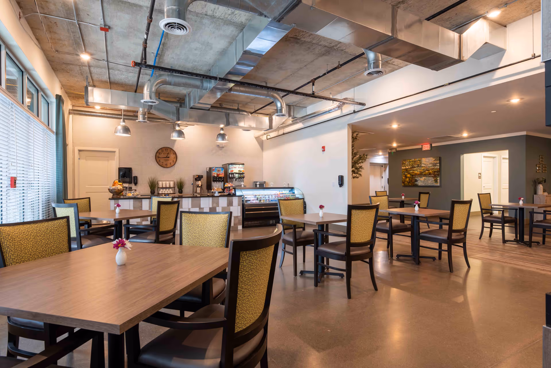 Spacious modern dining area with multiple tables and chairs, a service counter and exposed ceiling ducts.