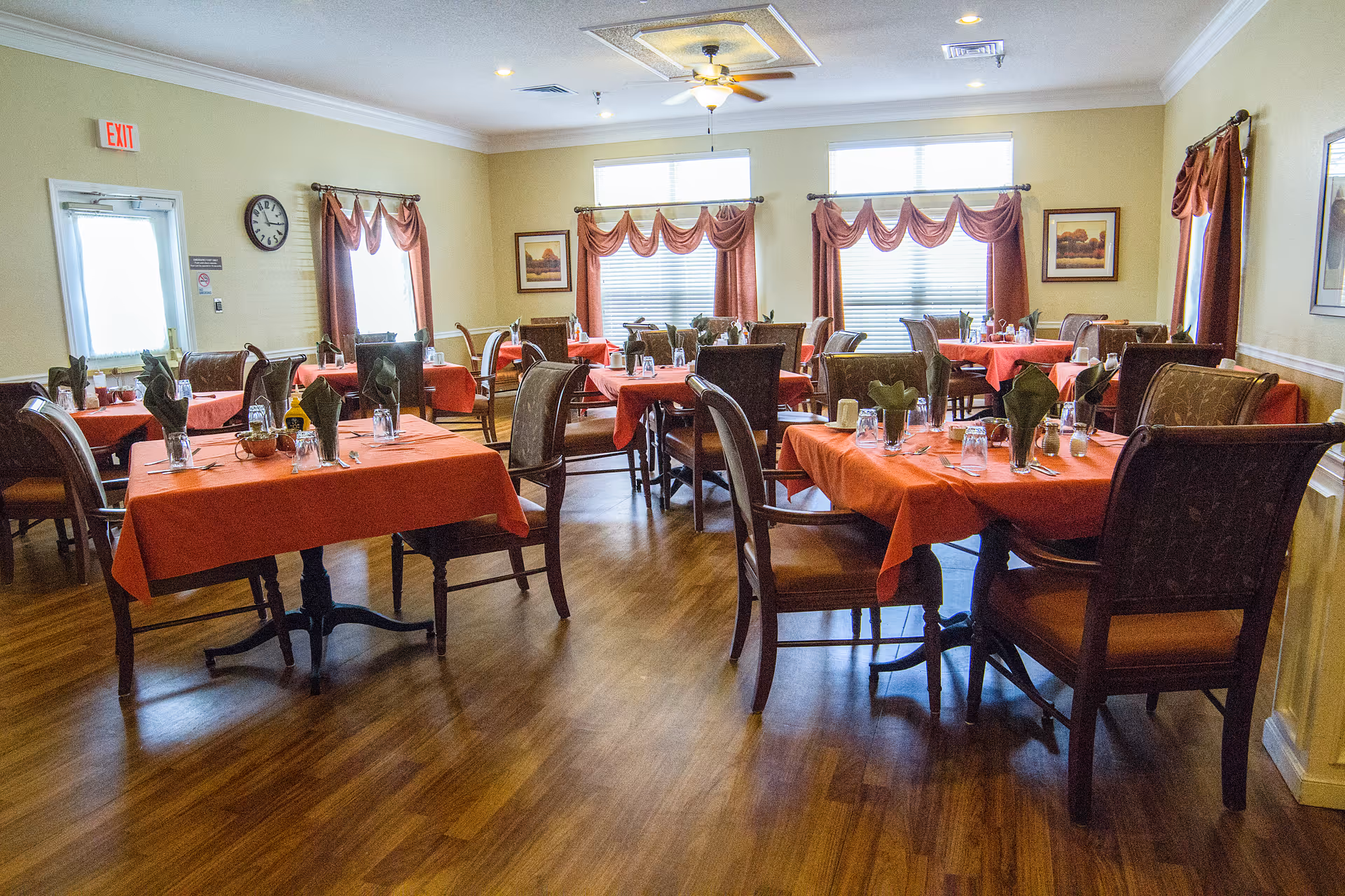 Dining room with multiple tables covered in red tablecloths and set with napkins and glassware.