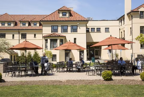 Outdoor courtyard of Villa Marie Claire with tables, umbrellas, and residents seated.