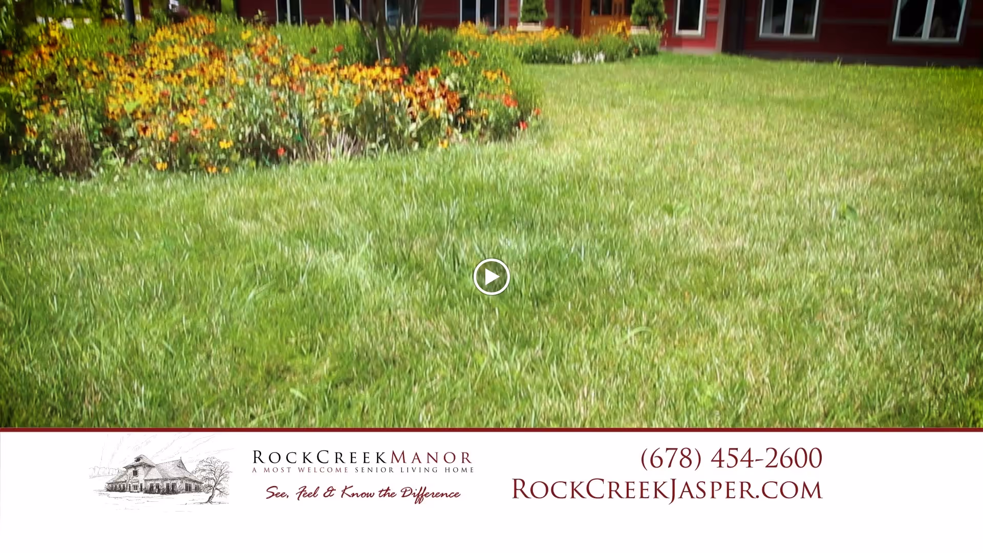 A well-maintained grassy lawn with a flower bed of yellow and orange flowers in front of a red building with multiple windows, likely part of a senior living facility.