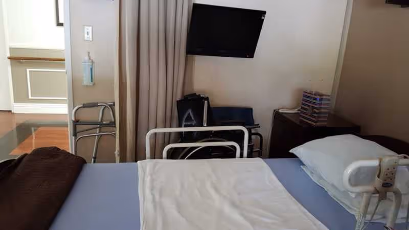 Interior senior facility patient room with hospital bed, curtain, TV, and medical equipment.