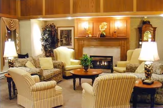 Comfortable senior living common room with upholstered chairs and sofas arranged around a fireplace and coffee table.
