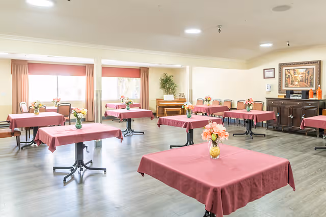 Communal dining room with square tables draped in burgundy tablecloths and small floral centerpieces.
