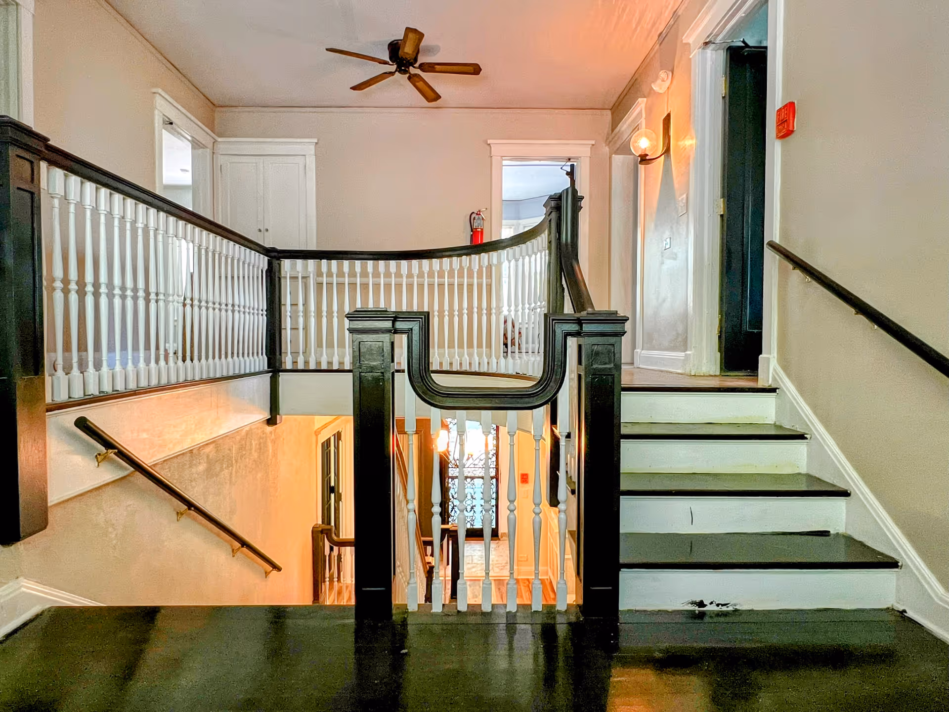 Interior stair landing with a black-and-white banister, staircase, ceiling fan and hallway doors.