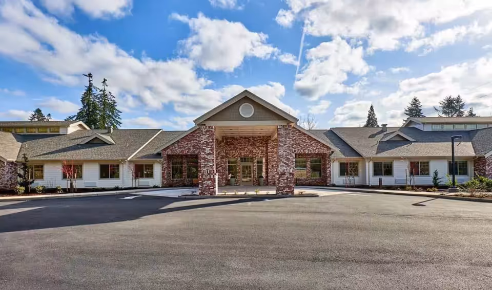 Front entrance of a single-story brick-and-siding building with a covered portico and circular driveway under a partly cloudy sky.