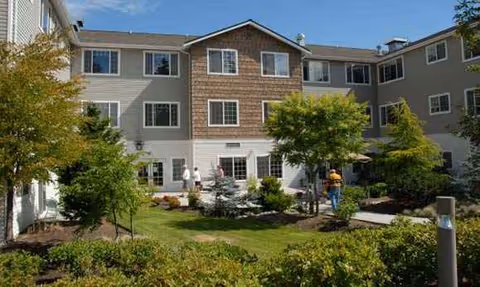 Two-story senior living building with a landscaped courtyard and residents walking.