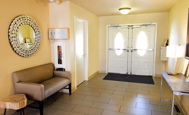 Bright entryway with double doors, a bench, round mirror, console table, and lamp.