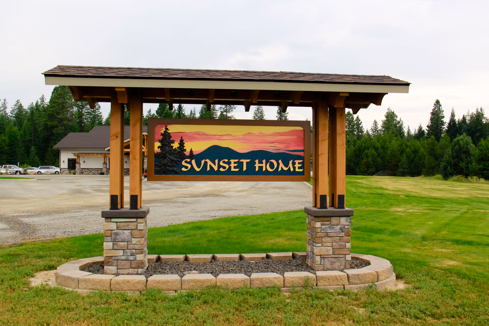 Wooden entrance sign reading 'SUNSET HOME' on a grassy lot with trees and a building in the background.