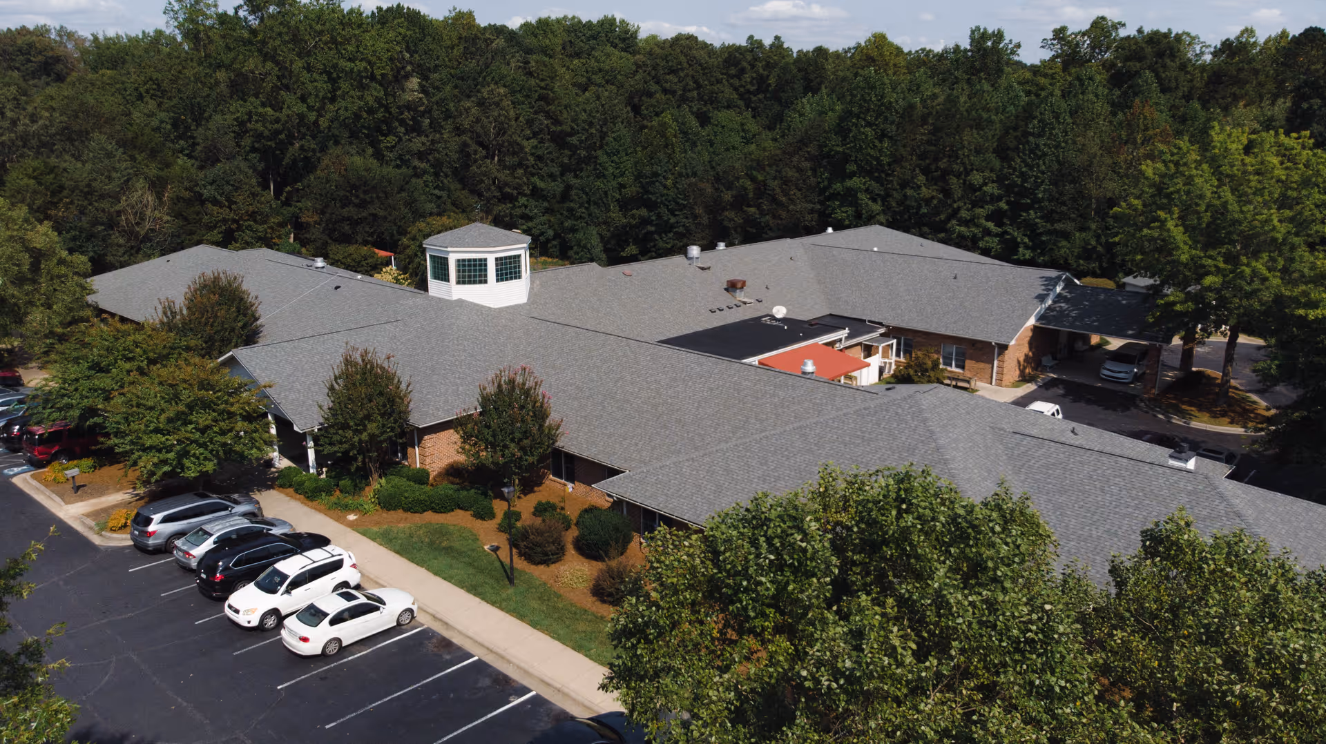 Aerial view of the Southfork senior living facility building surrounded by trees with a parking lot and several parked cars.