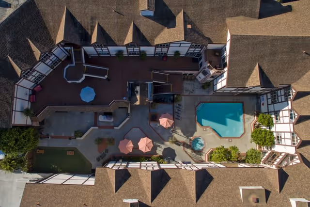 Aerial view of an enclosed courtyard at Lexington Assisted Living featuring a swimming pool, hot tub, patio umbrellas, seating areas and surrounding pitched-roof buildings.