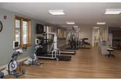 Rehabilitation gym room with treadmills, stationary bikes, strength machines, and wood-look flooring.