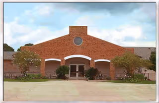 Brick building with three arched entrances and a circular window, surrounded by shrubs.