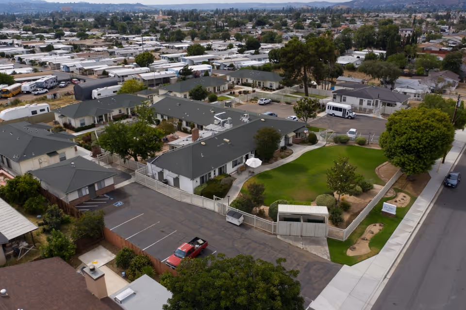 Aerial view of Lo-Har Senior Living showing single-story buildings surrounding a fenced green lawn, walkways and a parking lot with vehicles.