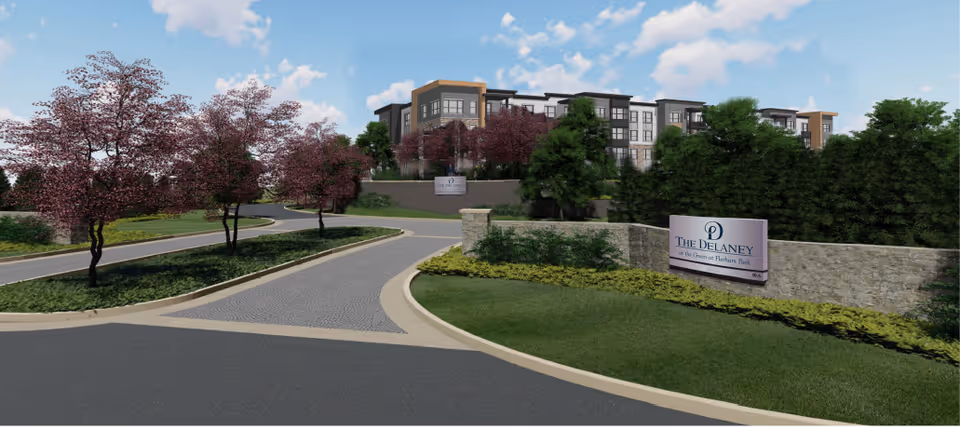 Curved entrance drive and landscaped grounds leading to a multi-story senior living building with a 'The Delaney' sign.