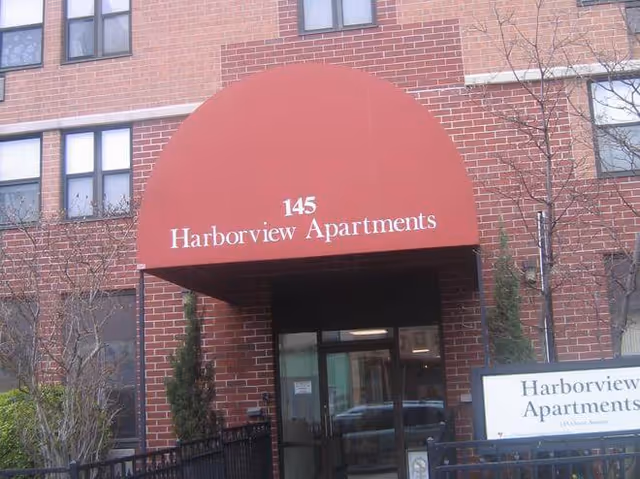 Brick apartment building entrance with a red curved awning labeled 'Harborview Apartments'.