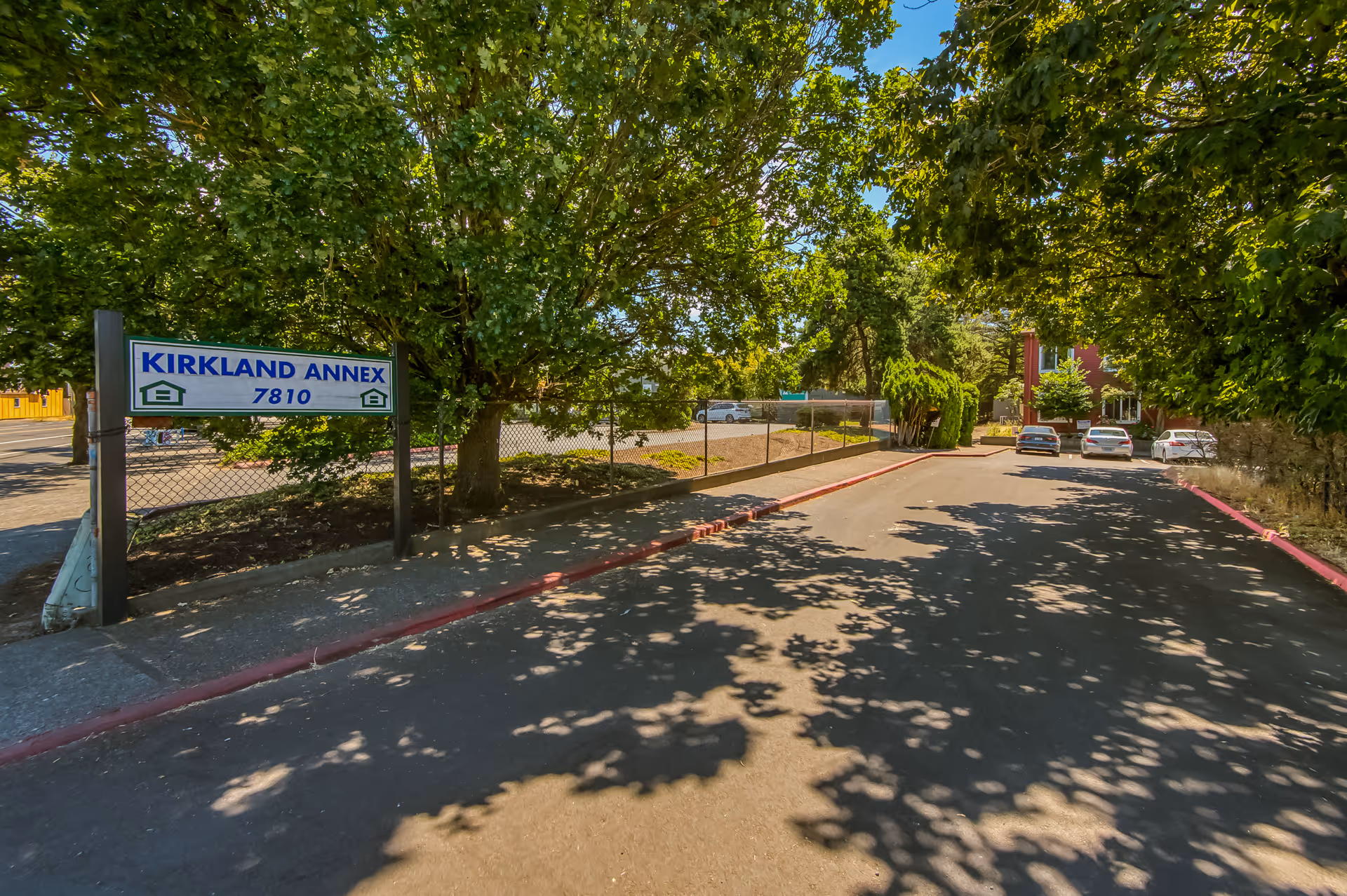 Entrance driveway to Kirkland Annex with a sign reading 'Kirkland Annex 7810', shaded by trees and leading to a parking area and building.