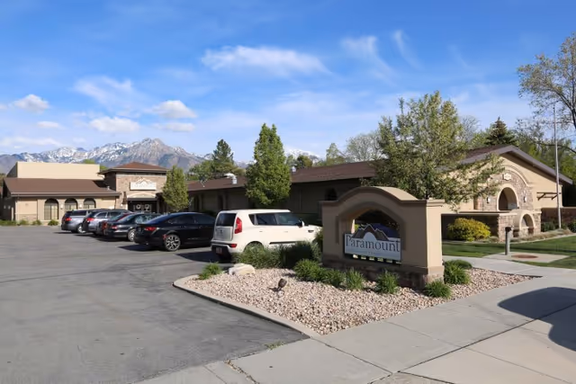 Front exterior of the Paramount Health and Rehabilitation building with a parking lot, facility sign, and mountains in the background.