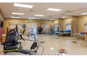 Spacious rehab and exercise room with stationary exercise equipment, therapy tables, and privacy curtains in a senior living facility.