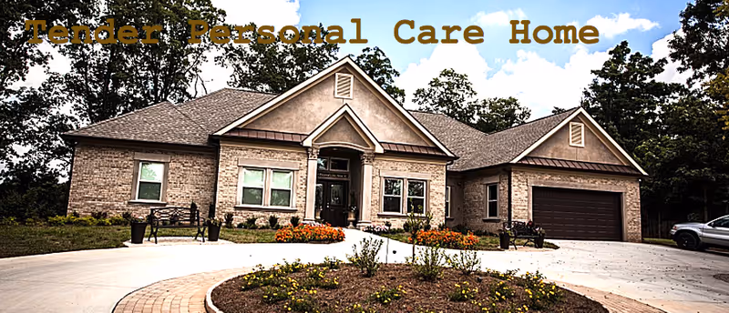 Front exterior view of a single-story brick house with a gabled roof, a driveway, a garage, and landscaped garden beds with flowers and shrubs under a partly cloudy sky.