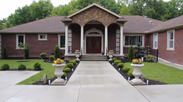 Front entrance of a single-story brick building with a concrete walkway, columns, double doors, and decorative planters.