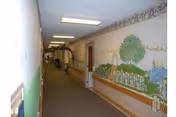 Long indoor hallway with mural-painted walls, ceiling lights, and doors along both sides.