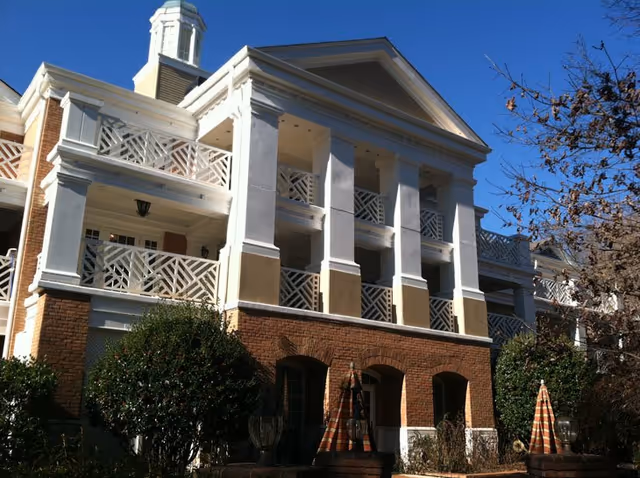 Front exterior of a multi-story brick building with white columns, balconies and a small cupola under a clear blue sky.