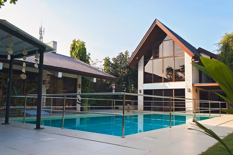 Outdoor swimming pool with a metal safety railing and a modern two-story building with a triangular glass facade in the background.