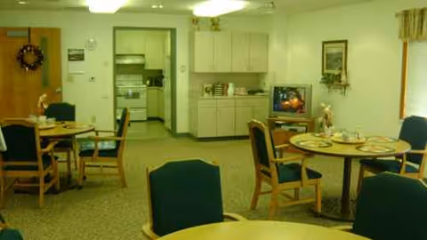 Common dining area with round tables, chairs, a small kitchen, and a TV in the corner.