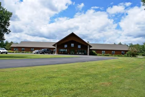 Single-story senior living facility with a peaked entrance, parking lot, and expansive green lawn.