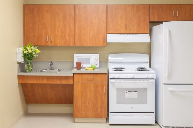Small kitchenette with wooden cabinets, a sink, microwave, white stove and refrigerator.