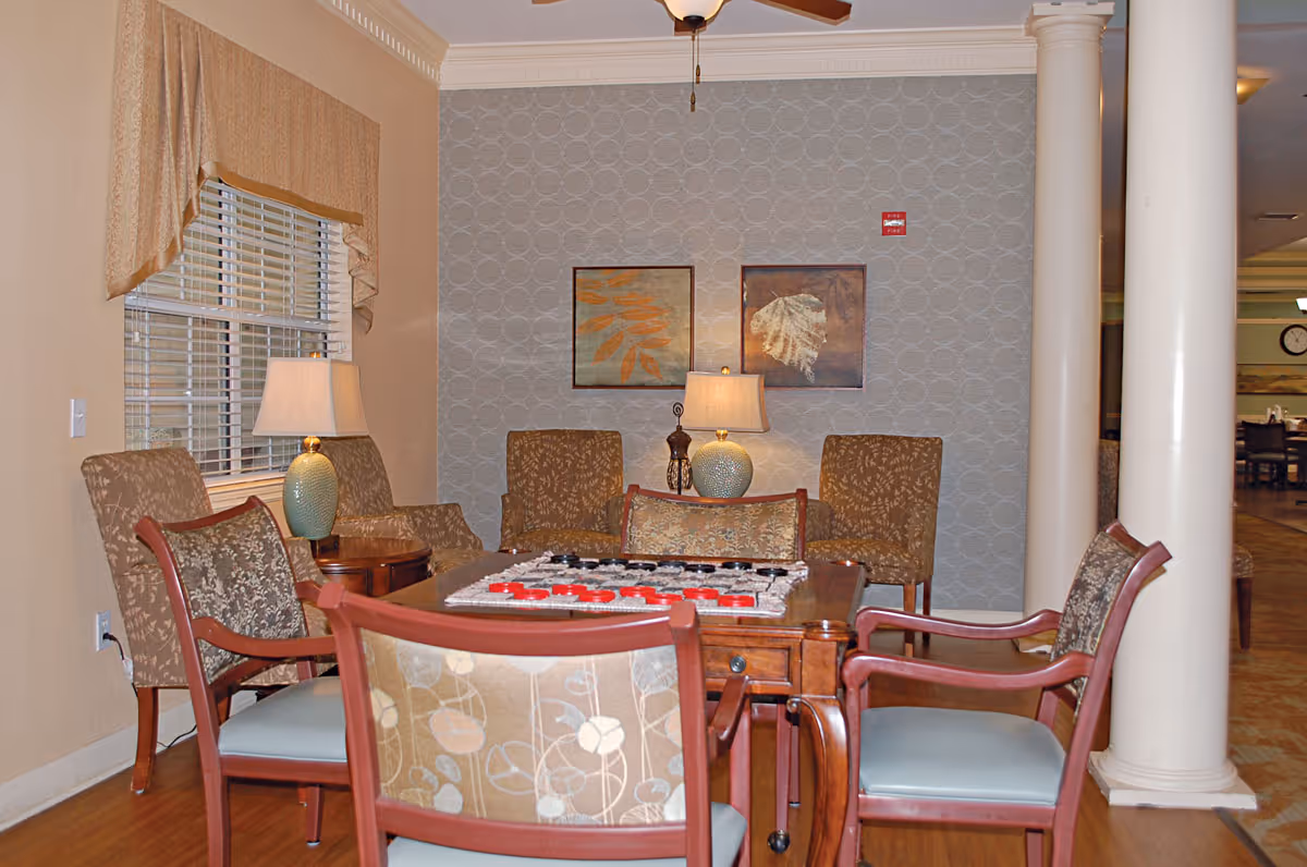 Cozy seating area with chairs around a game table, lamps, framed art, and decorative columns.