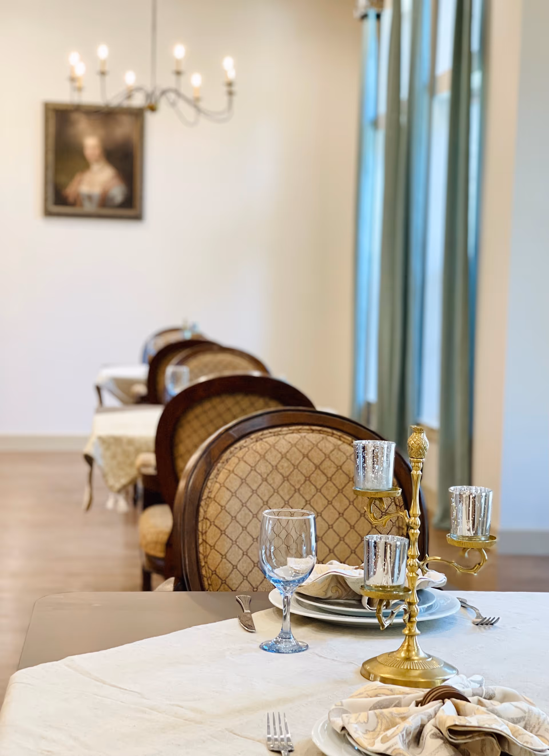 Elegantly set dining table with glassware, a brass candelabra, and upholstered chairs in a bright dining room.