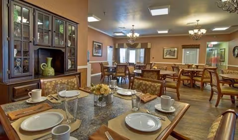 Dining room with several set tables, wooden chairs, chandeliers, and a china cabinet.