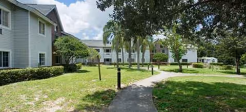 Outdoor walkway along a Brookdale Clinton residential building with green lawns and trees.
