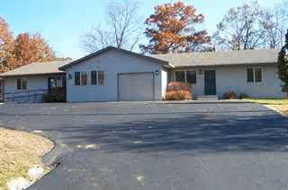 Exterior of a single-story senior living facility with garages, driveway, and autumn trees.