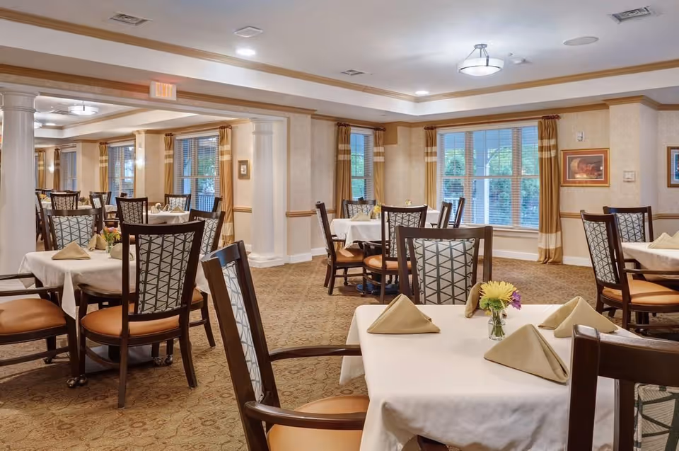 Bright, upscale dining room with multiple set tables, cushioned chairs, folded napkins and small floral centerpieces.