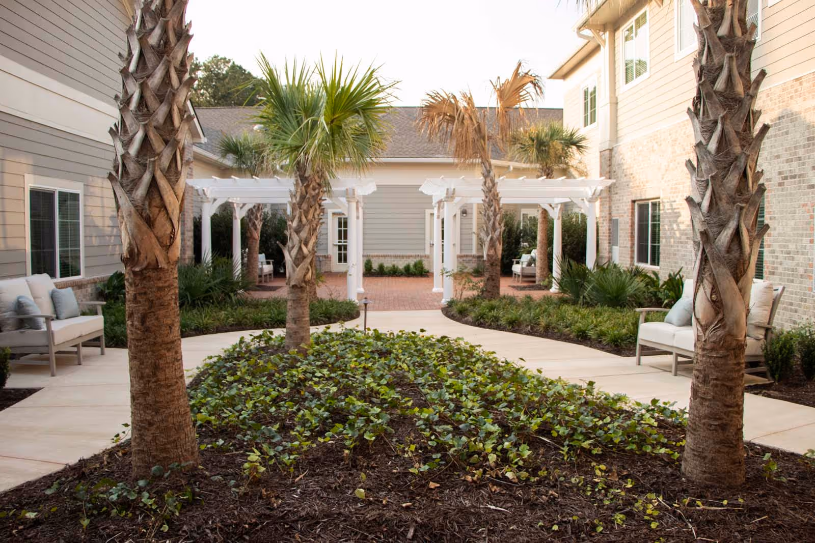 Central landscaped courtyard with palm trees, paved walkways, white pergolas, and outdoor seating between building wings.