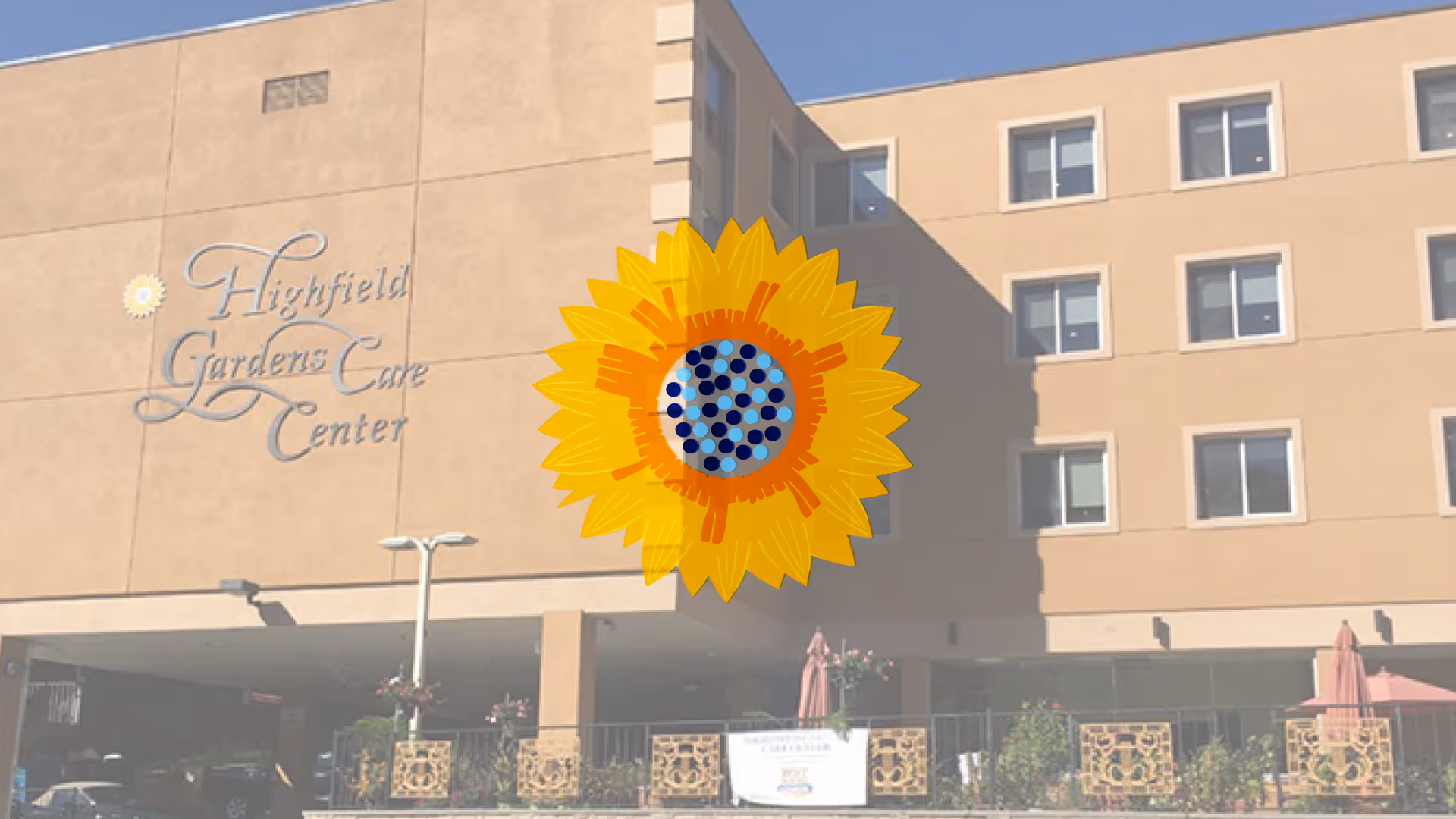 Exterior view of Highfield Gardens Care Center building with multiple windows and a covered entrance area. There are decorative railings and some outdoor plants visible near the entrance.
