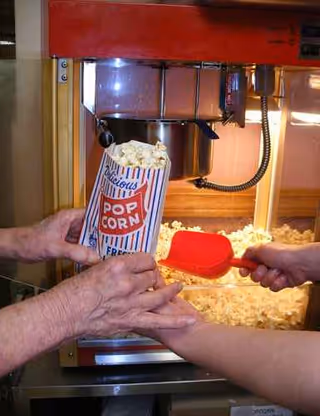 Two hands reach for popcorn from a popcorn dispenser in a kitchen.
