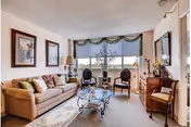 Bright furnished common living room with a sofa, two chairs by a large window, glass coffee table and decorative accents.