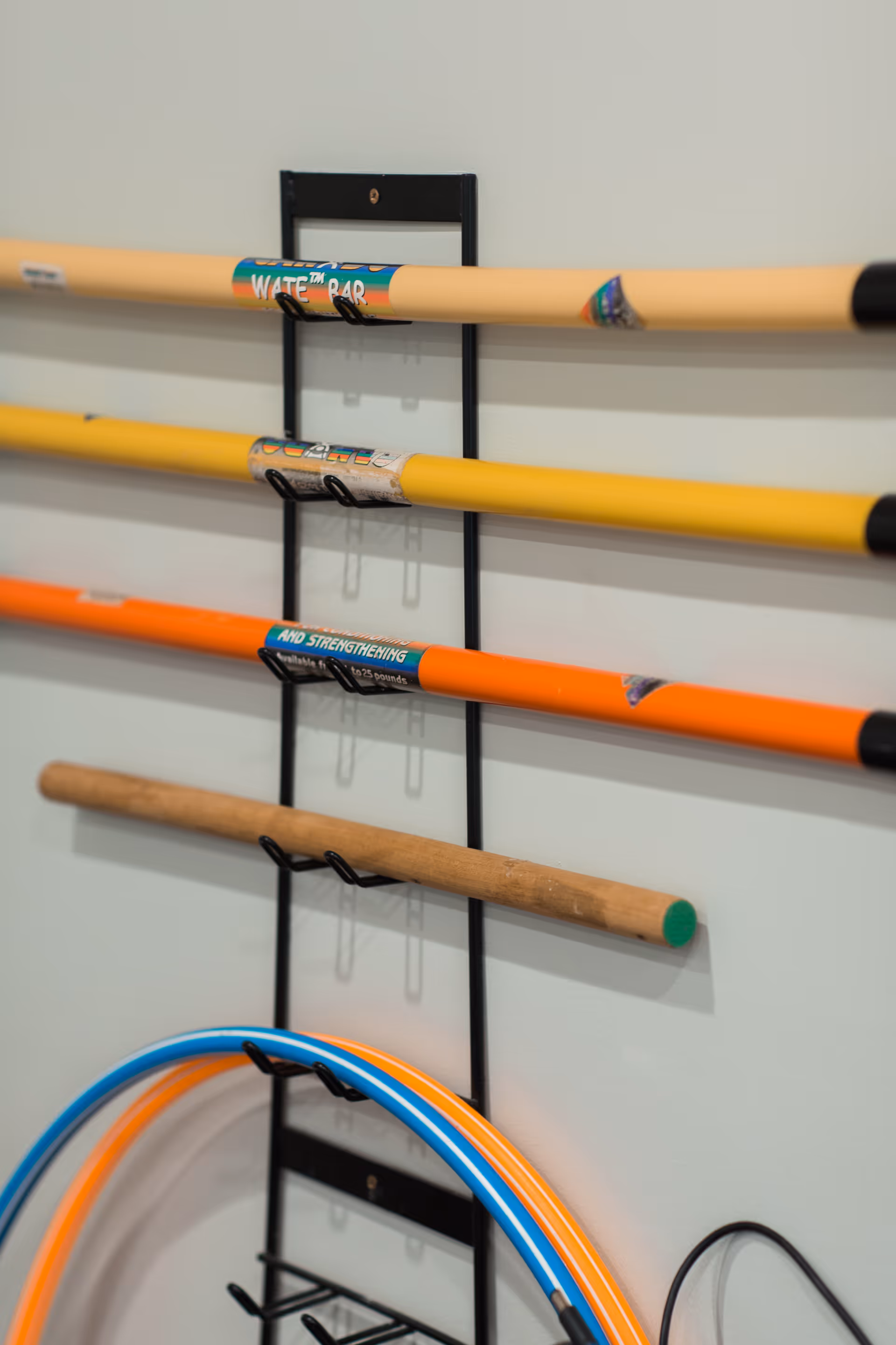 A wall-mounted rack holding several colorful exercise bars and hula hoops, used for physical therapy or fitness activities.