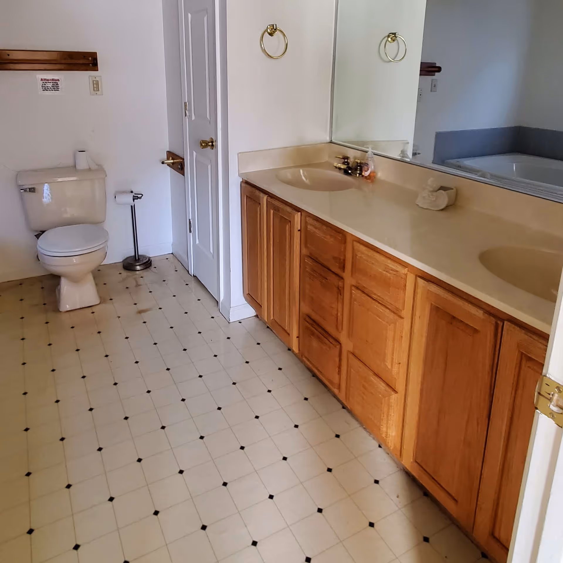 Bathroom with a double-sink vanity and wooden cabinets, a toilet, and a tiled floor.