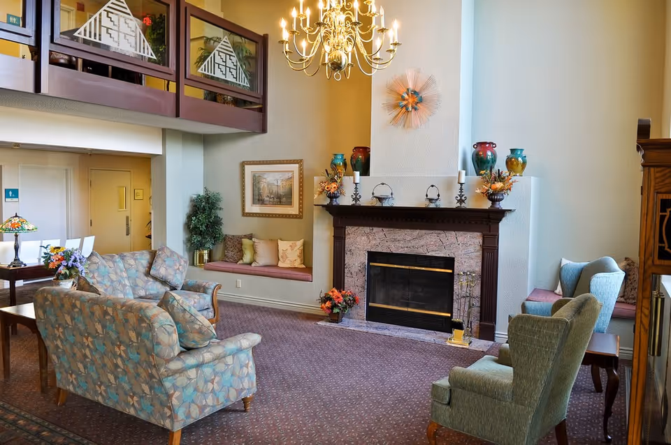 Spacious living room with upholstered sofas and chairs arranged around a fireplace beneath a chandelier.