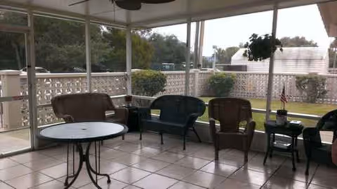 Screened outdoor seating area with chairs and a round table overlooking a yard.