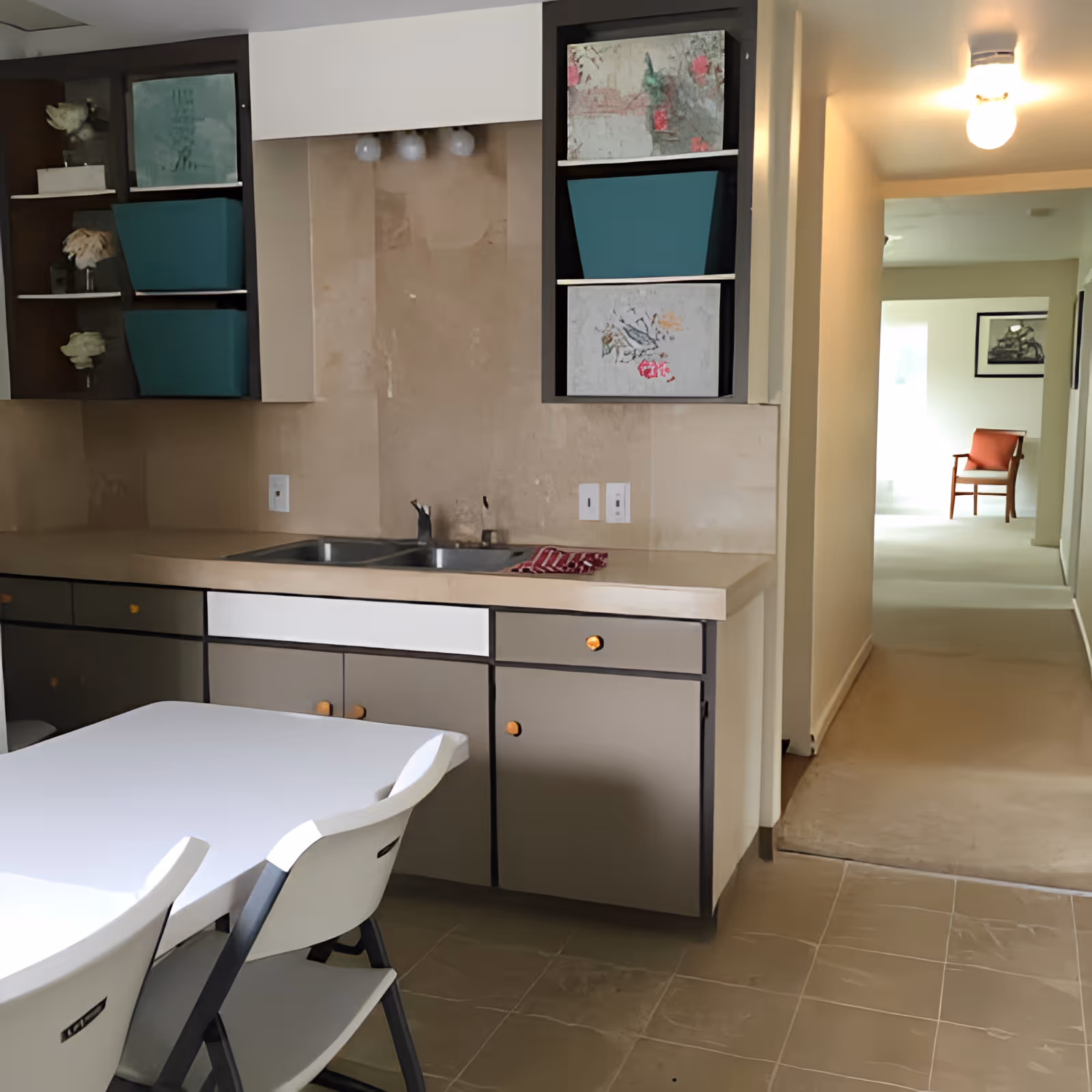 Kitchenette with a sink, cabinets and a folding table with chairs opening into a hallway with a chair visible at the end.