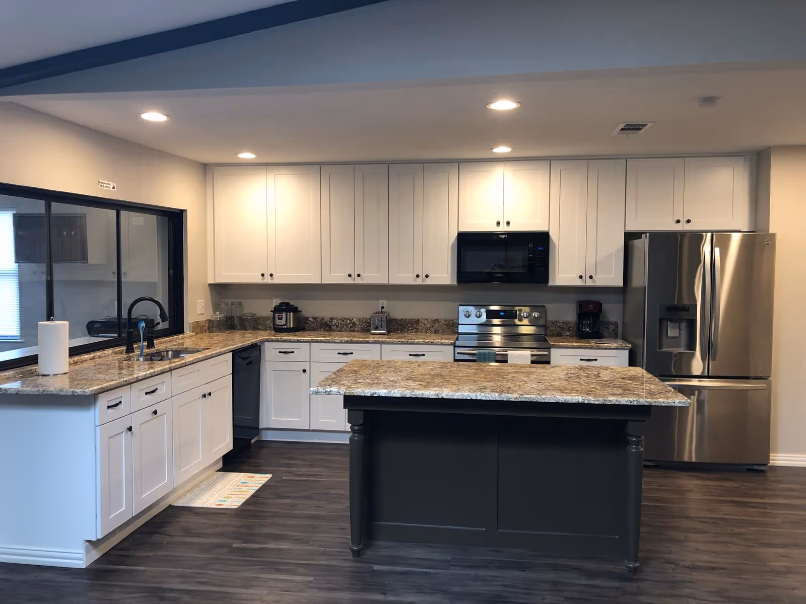 Bright, modern kitchen with white cabinets, granite countertops, island, and stainless steel appliances.