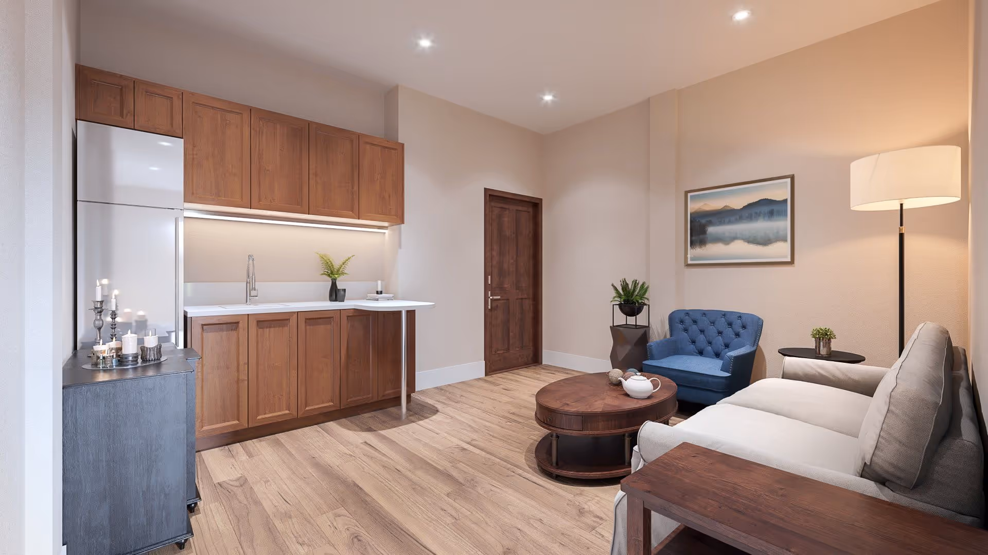 A cozy living area with a small kitchen featuring wooden cabinets and a white countertop. The room includes a blue armchair, a gray sofa, a round wooden coffee table with a teapot on it, a floor lamp, and a framed landscape picture on the wall. The floor is wooden, and there is a wooden door in the background.