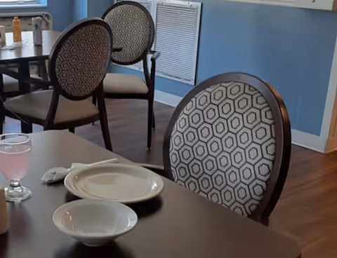 Dining room table with plates, a bowl, a glass of pink drink and patterned chairs in a communal dining area.