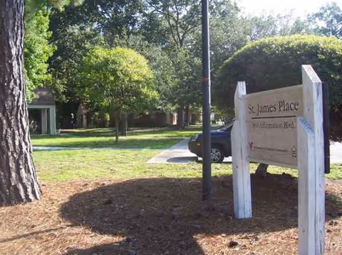 Exterior view of St James Place entrance sign among trees with a parked car nearby.