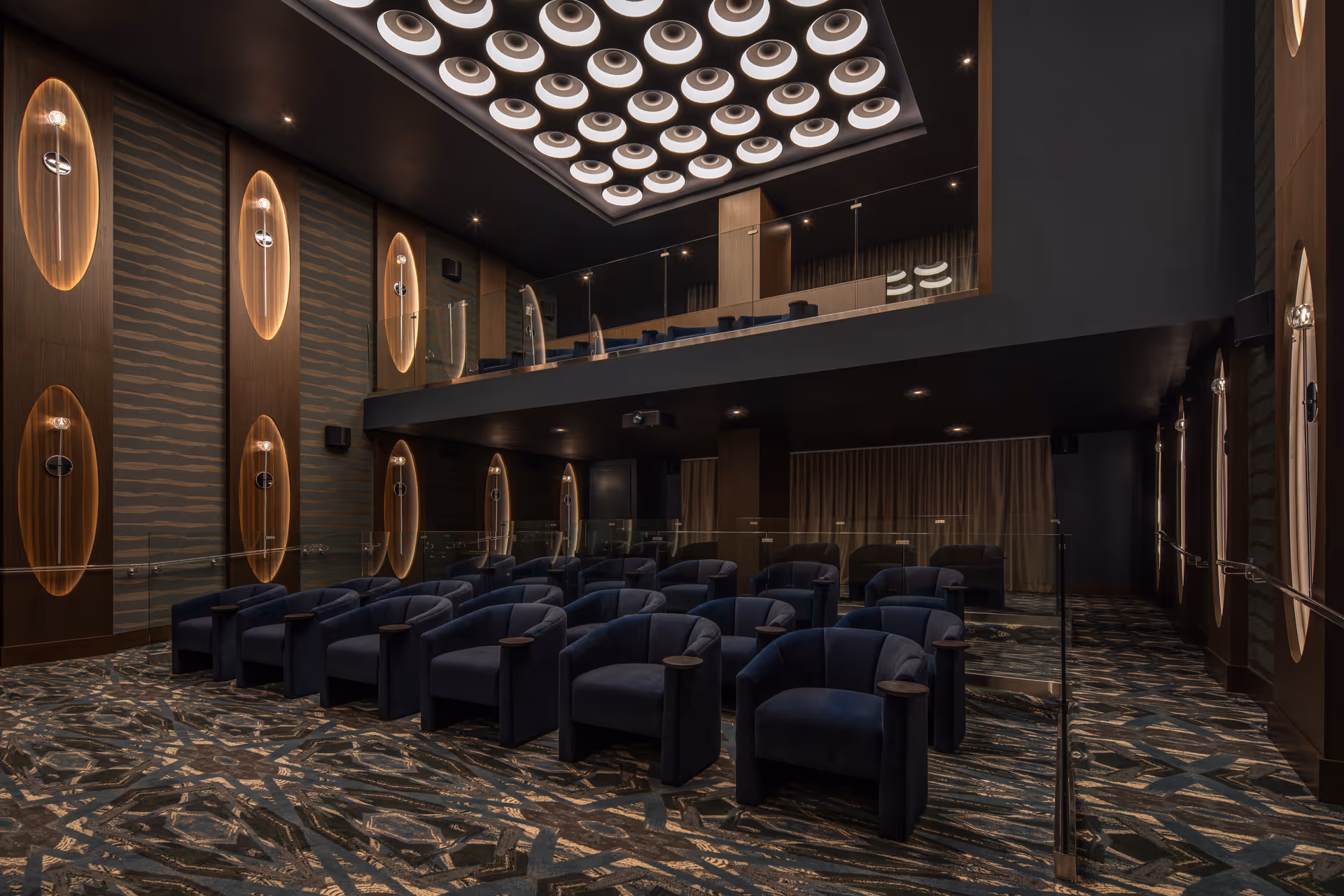 A luxurious theater/screening room with rows of navy upholstered armchairs, a balcony, and modern ceiling and wall lighting.